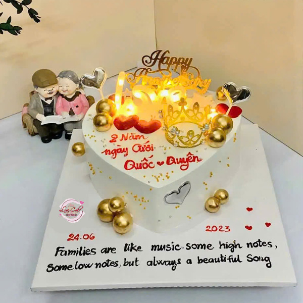 Bánh kem kỷ niệm ngày cưới hình trái tim màu trắng trang trí vương miện, trái tim ánh kim và nến lãng mạn dành cho các cặp đôi.
